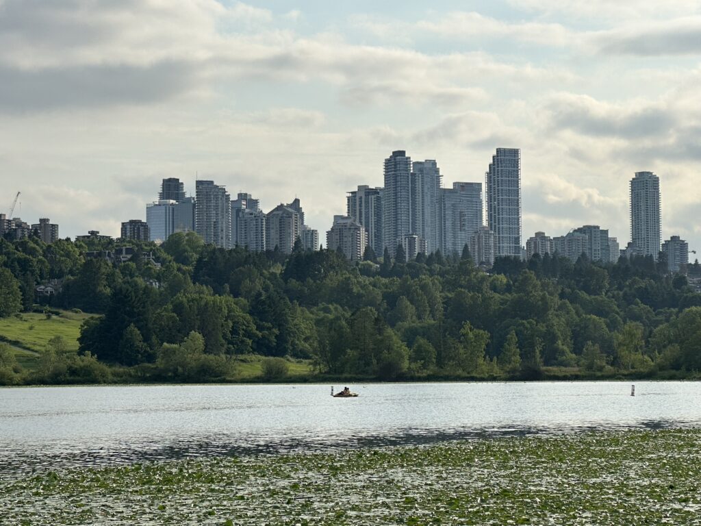 Tower buildings of the Metrotown are overlooking Deer Lake, with someone paddling in a canoe 