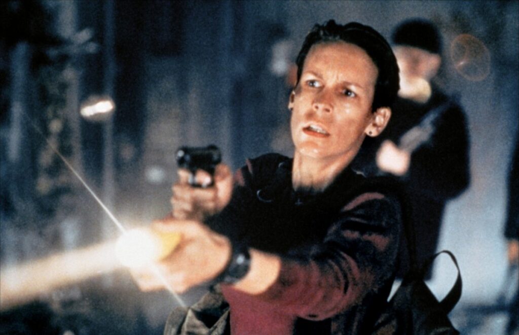 Jamie Lee Curtis holding a gun and a flashlight, looking for the, err, virus, I guess.