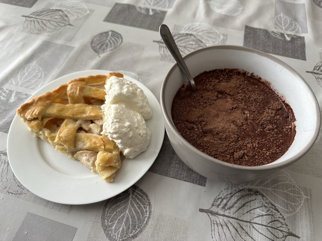 A slice of apple pie with whipped cream, and a bowl of hot chocolate 