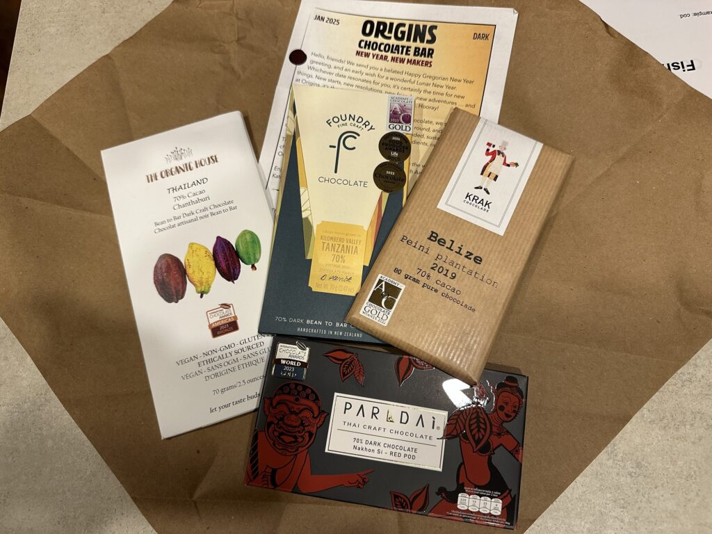 Four chocolate bars, along with the Origins Chocolate Bar flyer for this month's delivery.

- The Organic House, 70% Thailand
- Foundry, 70% Tanzania
- Krak 70% Belize
- Parldai (?) 70% Thailand (?)