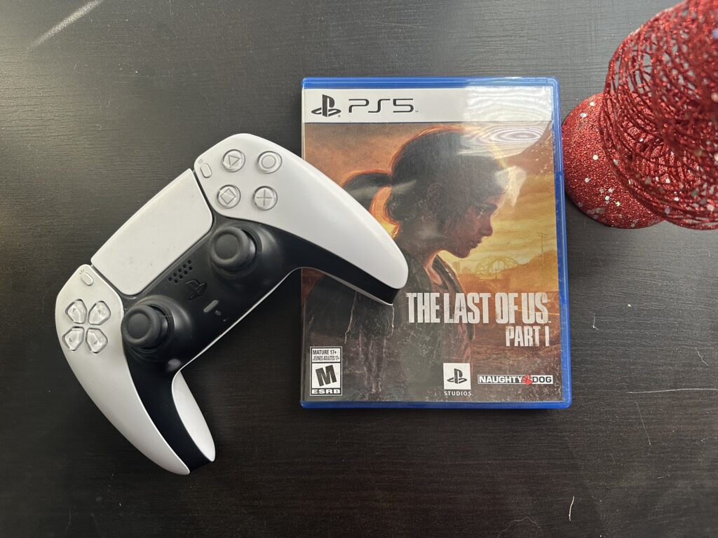 A picture of a PS5 controller and the game box for "The Last of Us" (part 1)