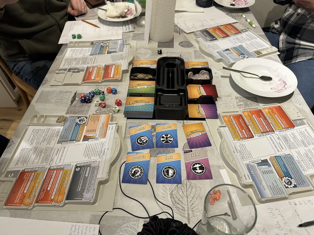 Table with a whole bunch of Spectaculars cards, dice, and character sheets... plus some empty plates from eating apple and/or blueberry pies!