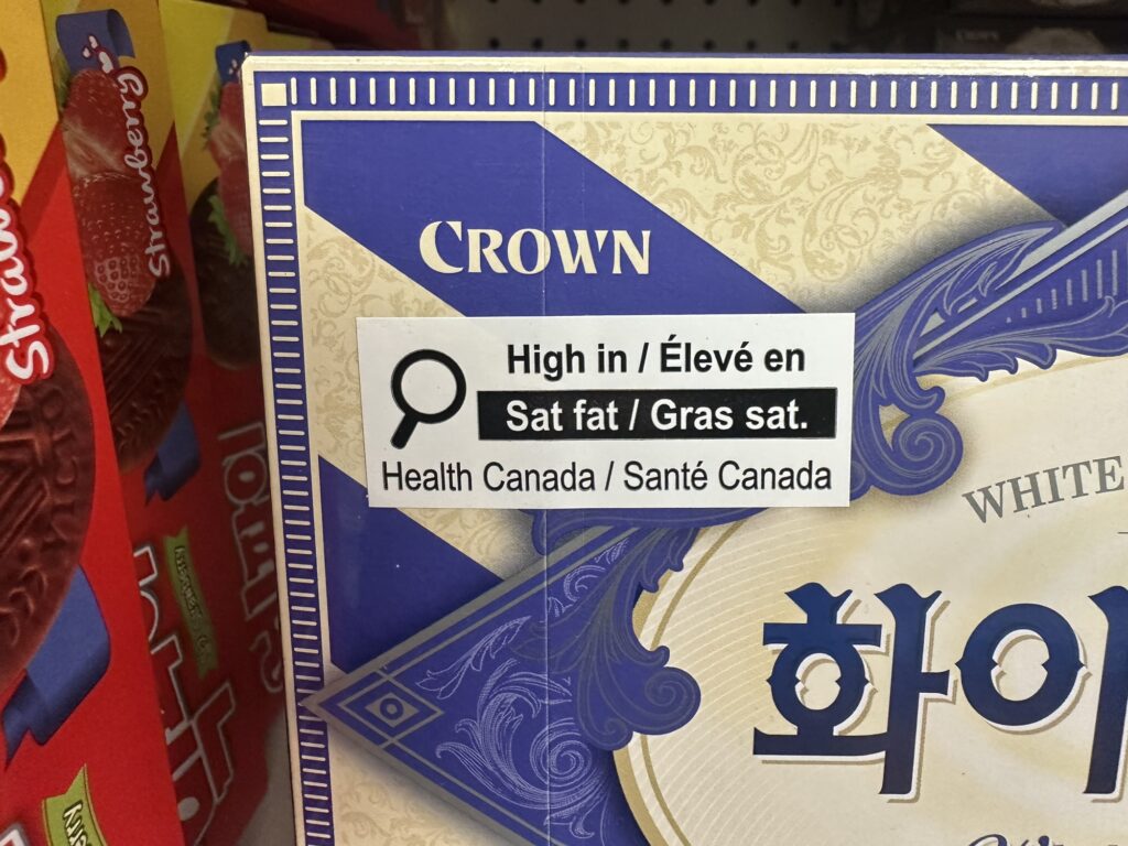 A "helpful" sticker from Health Canada that indicates how junk food has "high levels of saturated fat" (other items on the shelf had similar stickers for other things like sugar and so on)