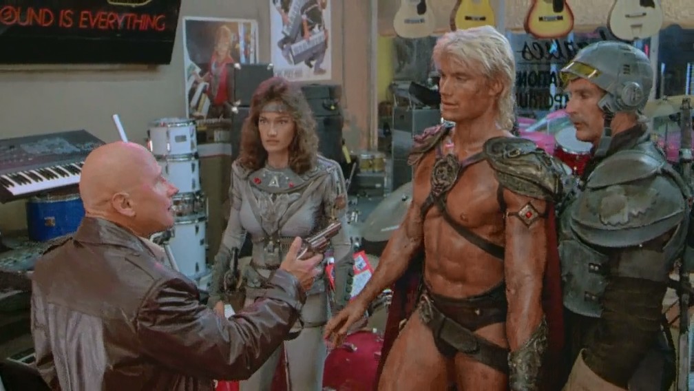Detective Lubic (James Tolkan) points a gun at He-Man (Dolph Lundgren) in the 1987 movie "Masters of the Universe"