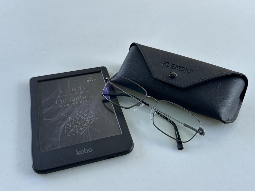 A pair of Flexon glasses (with the case) on a white table. There's also a Kobo e-reader, currently set on Asimov's "Foundation and Empire".
