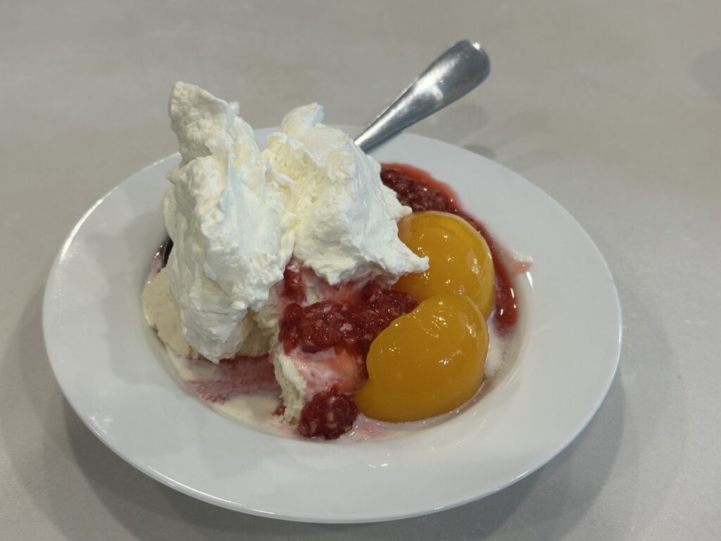 A hastily homemade Peach Melba, which is vanilla ice-cream, raspberry coulis, peach halves, and whipped cream.