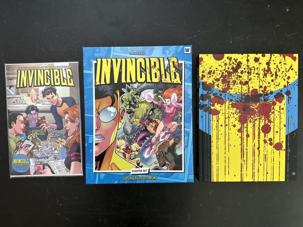The Invincible Kickstarter loot: the core rulebook with the special cover, the Starter Set box, and the first issue of the original comic, but with a new cover.